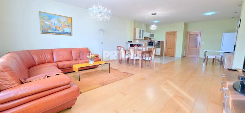 VEĽKOMETRÁŽNY 3i byt, 3 x NEPRIECHODNÁ IZBA, KLÍMA, BALKÓN, Nám.SNP - Obývacia izba s podlahou s dreveným dekorom, kožený gauč, jedálenský stôl, kuchyňa v 3-izbovom byte.