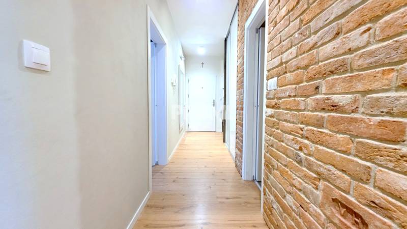 LUXUSNÝ 3i byt, TERASA, PARKING, KLÍMA, ZELENÁ HORKA, Ďumbierska ulica - Chodba v 2-izbovom byte s tehlovou stenou a podlahou s dreveným dekorom.