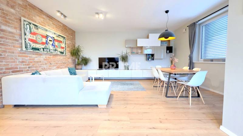 LUXUSNÝ 3i byt, TERASA, PARKING, KLÍMA, ZELENÁ HORKA, Ďumbierska ulica - Obývačka s bielym nábytkom, podlaha s dreveným dekorom, tehlová stena, obraz bankovky.