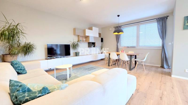 LUXUSNÝ 3i byt, TERASA, PARKING, KLÍMA, ZELENÁ HORKA, Ďumbierska ulica - Obývacia izba s bielym gaučom a televíziou v 2-izbovom byte, podlaha s dreveným dekorom.