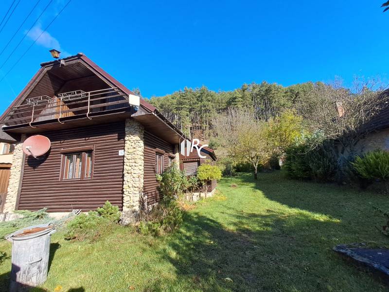 Šikovná drevenica pod lesom Slovenské Pravno  - Rodinný dom v Slovenskom Pravne z dreva a kameňa, strom, zeleň, modrá obloha.