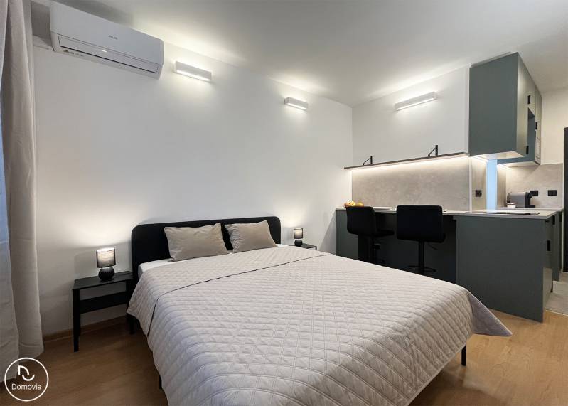 Bez provízie | Na prenájom dizajnové štúdio v Ružinove - Spálňa s podlahou s dreveným dekorom, dvojposteľou a kuchynským kútom v garsónke.