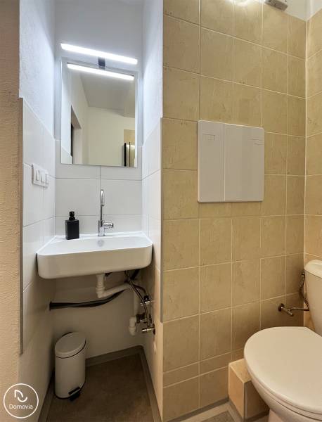 Bez provízie | Na prenájom dizajnové štúdio v Ružinove - Kúpeľňa v garsónke s umývadlom, zrkadlom a toaletou, svetlá dlažba na stene.