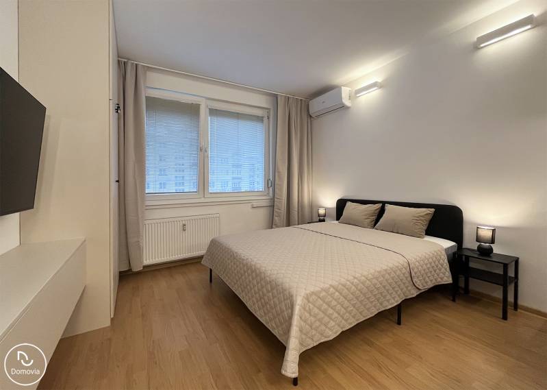 Bez provízie | Na prenájom dizajnové štúdio v Ružinove - Spálňa v garsónke s posteľou, klimatizáciou a podlahou s dreveným dekorom.