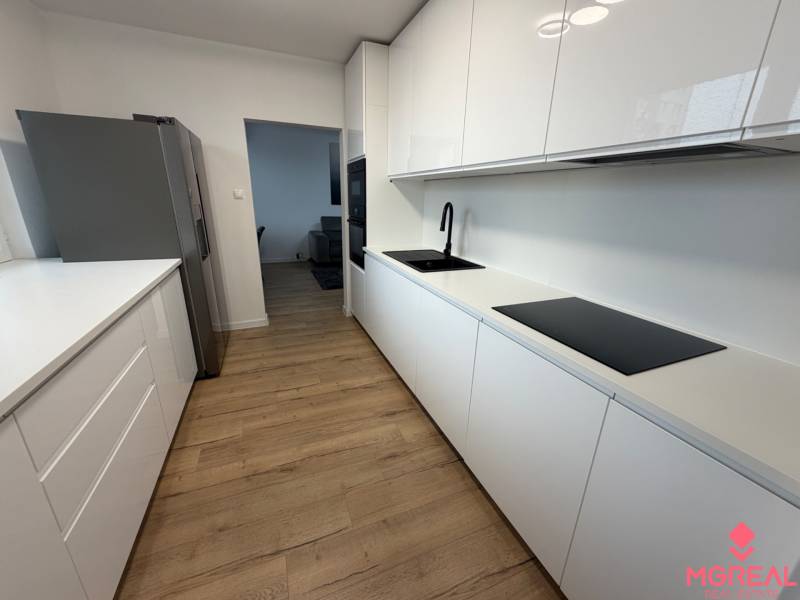 3 izbový byt s balkónom Topoľčany / PRENAJOM  - Kuchyňa v 3-izbovom byte s podlahou s dreveným dekorom a bielymi skrinkami.