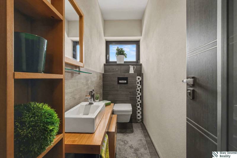 Ideálny dom pre rodinu, Blatné, okr. Senec - Kúpeľňa v rodinnom dome s keramickým umývadlom, drevodekor, polica a rastliny.