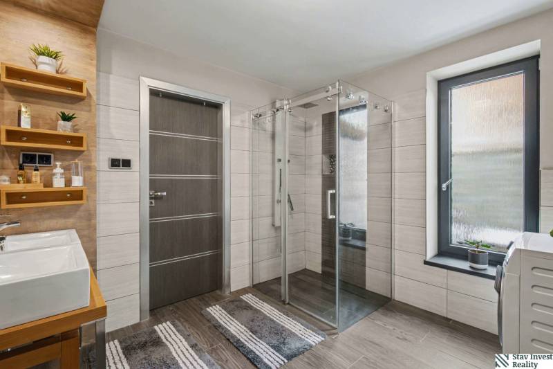 Ideálny dom pre rodinu, Blatné, okr. Senec - Kúpeľňa Rodinného domu s presklenou sprchou, pultom s umývadlom a podlahou s dreveným dekorom.