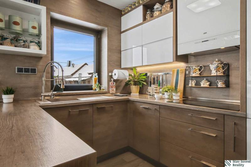 Ideálny dom pre rodinu, Blatné, okr. Senec - Kuchyňa v rodinnom dome s podlahou s dreveným dekorom, rastliny a poličky s čajovými súpravami.