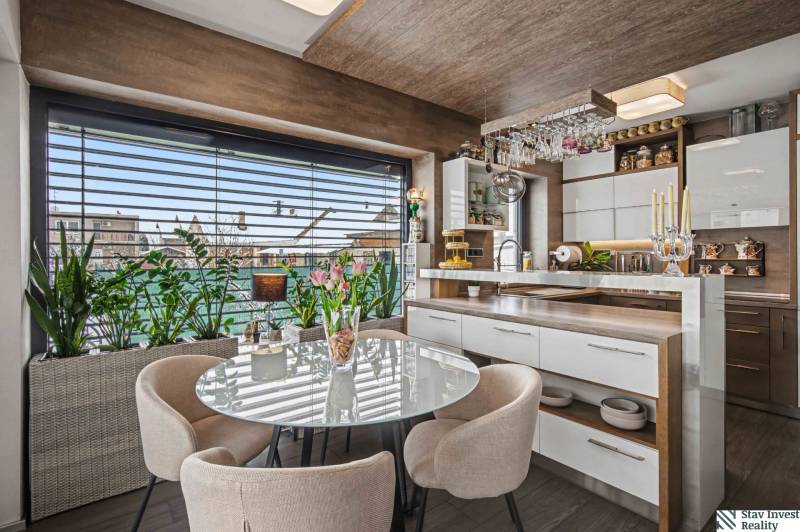 Ideálny dom pre rodinu, Blatné, okr. Senec - Kuchyňa v rodinnom dome s presklením, rastlinami a stolom s kreslami, podlaha s dreveným dekorom.