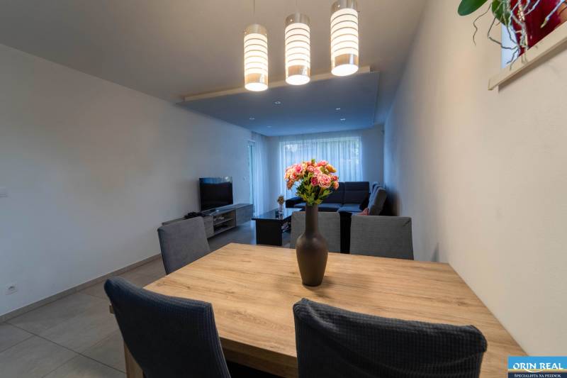 ATRAKTÍVNY 2 IZBOVÝ BYT S VLASTNOU ZÁHRADKOU a 3 parkovacími miestami - Jedálenský stôl s vázičkou, čierna sedačka a TV súčasťou 2-izbového bytu.