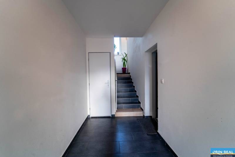 ATRAKTÍVNY 2 IZBOVÝ BYT S VLASTNOU ZÁHRADKOU a 3 parkovacími miestami - Chodba s tmavou dlažbou a schodmi, vedie k dverám s kvetinou na poschodí.