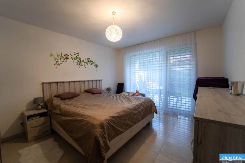 ATRAKTÍVNY 2 IZBOVÝ BYT S VLASTNOU ZÁHRADKOU a 3 parkovacími miestami - Spálňa 2-izbového bytu s posteľou, dekorom na stene a presklenými dverami.