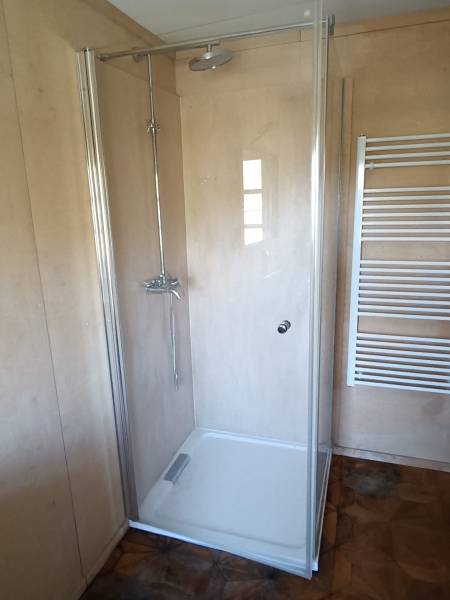 Na predaj záhradná chatka - Sprchový kút s presklenými dverami a rebríkovým radiátorom v chate na podlahe s dreveným dekorom.