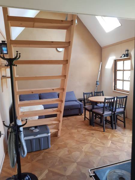 Na predaj záhradná chatka - Interiér chaty s podlahou s dreveným dekorom, sedačkou, schodmi a stolom so stoličkami.
