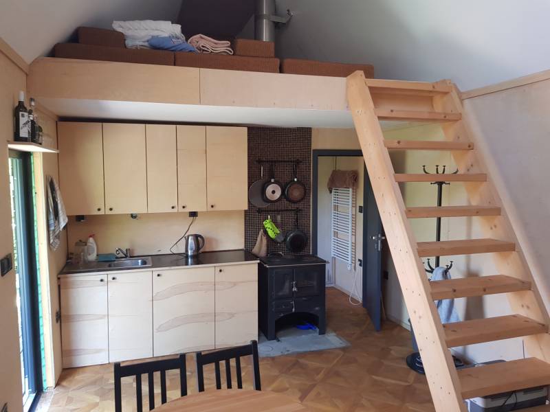 Na predaj záhradná chatka - Interiér chaty s kuchynkou, schodmi na poschodie a podlahou s dreveným dekorom.