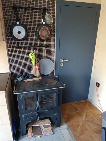 Na predaj záhradná chatka - Krbová pec v Chate s riadmi na čiernej stene, podlaha s dreveným dekorom.