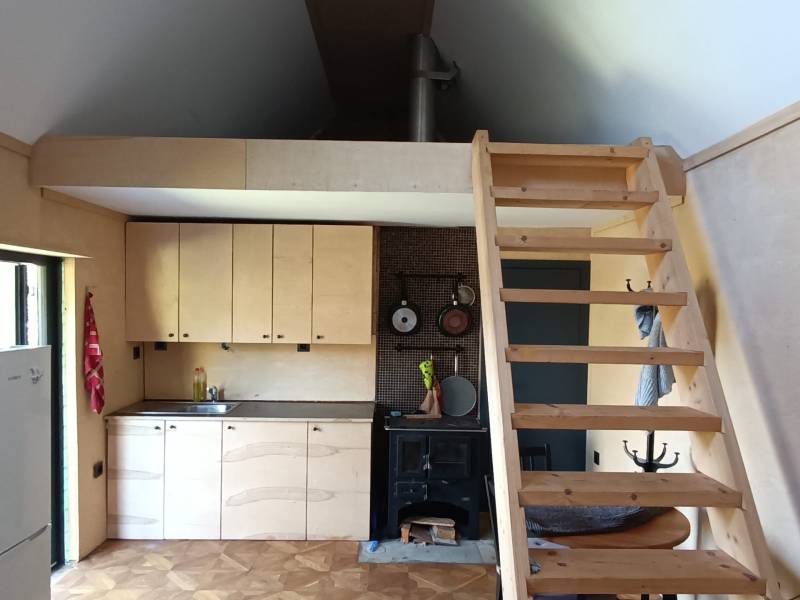 Na predaj záhradná chatka - Kuchyňa na Chate s drevenou podlahou dekoru, rebrík vedie na poschodie.