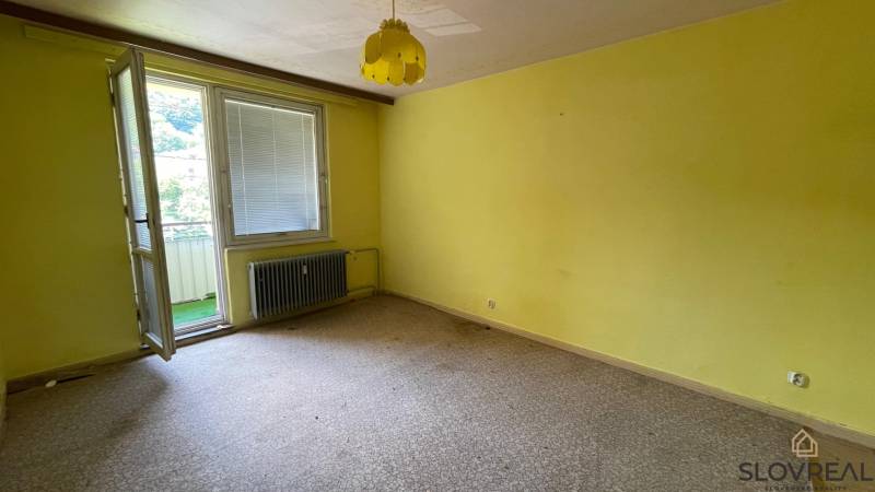 Na predaj veľký 3-izbový byt s lodžiou v Detve - Novosady - Izba v 3-izbovom byte so žltými stenami, otvoreným balkónom a radiátorom.