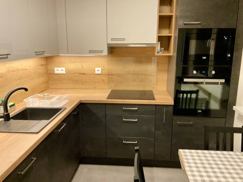 I Prenájom moderne zariadeného 3-izbového bytu v Petržalke. - Kuchynská linka v 3-izbovom byte s drevenými dekormi, čiernym drezom a zabudovanými spotrebičmi.