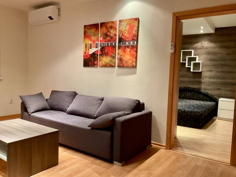 I Prenájom moderne zariadeného 3-izbového bytu v Petržalke. - Obývacia izba so šedou sedačkou, konferenčným stolíkom a podlahou s dreveným dekorom v 3-izbovom byte.