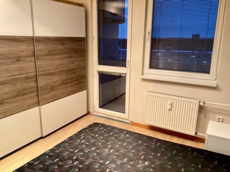 I Prenájom moderne zariadeného 3-izbového bytu v Petržalke. - Interiér 3-izbového bytu s podlahou s dreveným dekorom, šatníkovou skriňou a balkónovým oknom.