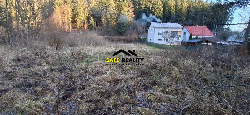 Stavebný pozemok Svrčinovec - Pozemky na bývanie v Svrčinovci, lúka s domami a lesom v pozadí.