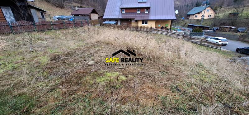 Lukratívny stavebný pozemok - Pozemok na bývanie v Oščadnici so svahovitým terénom a susednými domami v pozadí.