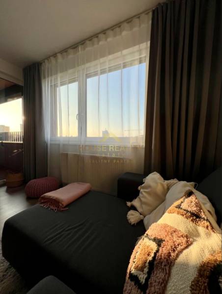 Novostavba FUXOVA 2 izbový byt, parking, Bosákova ul., BA V. Petržalka - Obývacia izba 2-izbového bytu s pohovkou, vankúšmi a záclonami.