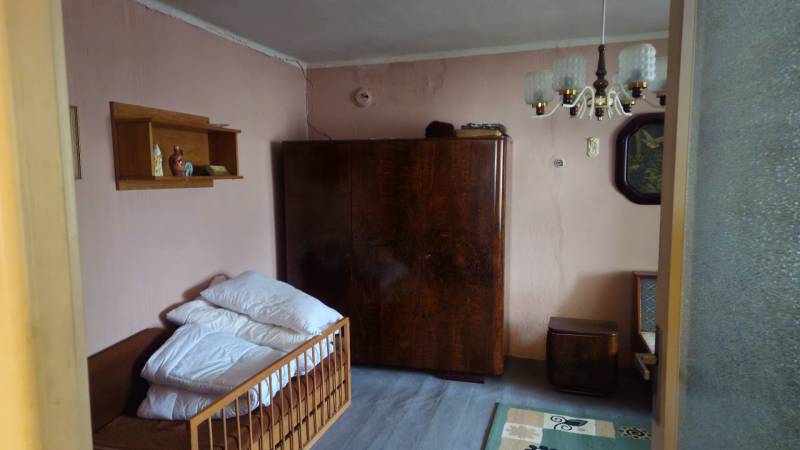 Predaj 4 izbový rodinný dom Šulekovo  - Izba rodinného domu s pohovkou, skriňou, lustrom a poličkou na stenách.