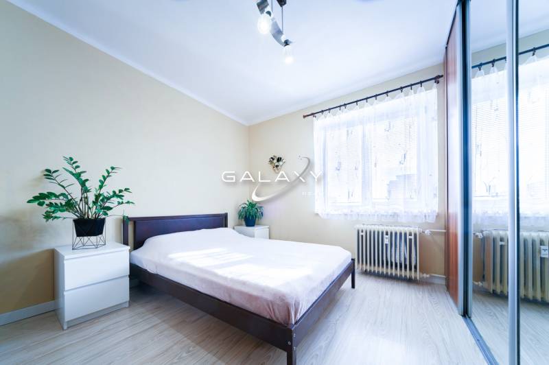 Kompletne zrekonštruovaný 3-izbový byt s balkónom – Rimavská Sobota - Svetlá spálňa s posteľou, zrkadlovou skriňou a podlahou s dreveným dekorom v 3-izbovom byte.