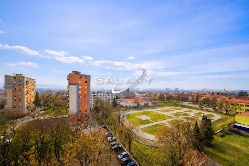 Kompletne zrekonštruovaný 3-izbový byt s balkónom – Rimavská Sobota - Výhľad z 3-izbového bytu na Rožňavskej ulici v Rimavskej Sobote, vysoké bytové domy, parkovisko.