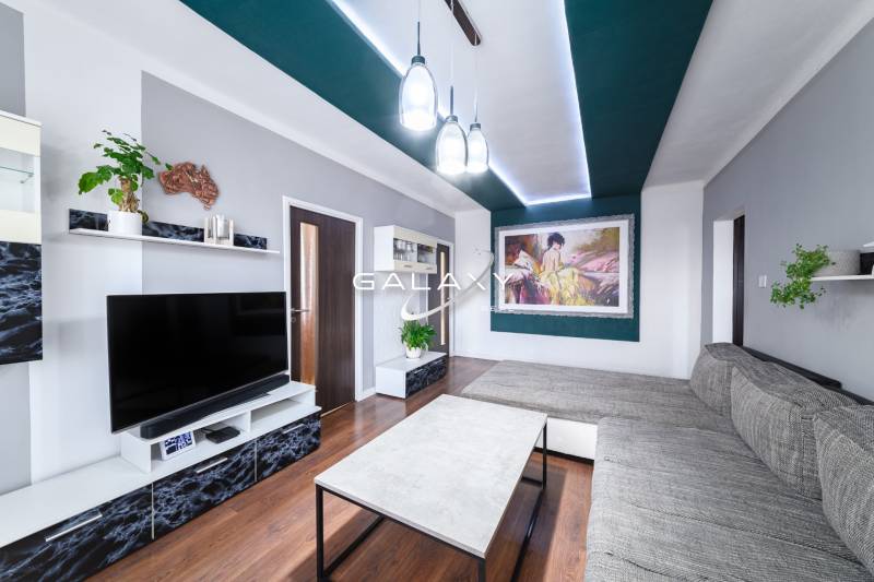 Kompletne zrekonštruovaný 3-izbový byt s balkónom – Rimavská Sobota - Obývačka v 3-izbovom byte s podlahou s dreveným dekorom, moderným nábytkom a umeleckým obrazom.