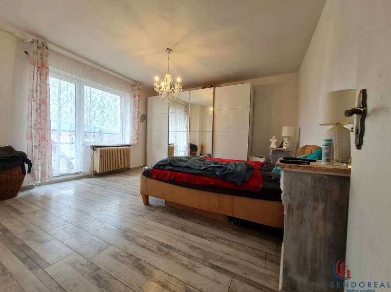 5.izb RD Čereňany pozemok 1028m - Svetlá spálňa s lusterom, veľkým oknom a podlahou s dreveným dekorom v rodinnom dome.