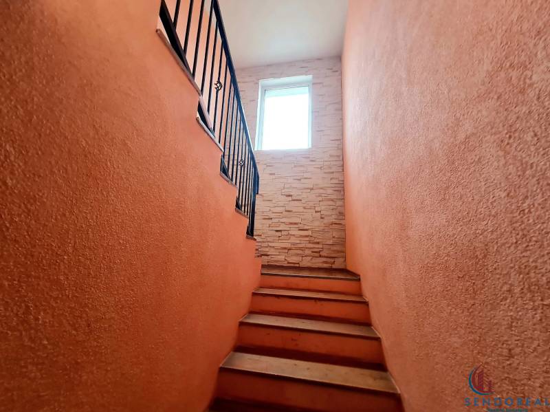 5.izb RD Čereňany pozemok 1028m - Schodisko v rodinnom dome s tehlovou stenou a oknom na konci.