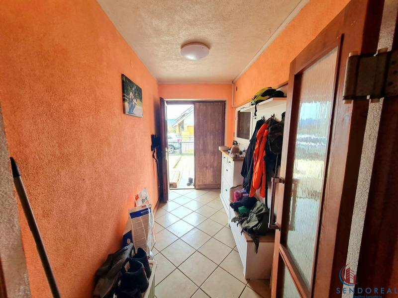 5.izb RD Čereňany pozemok 1028m - Chodba v rodinnom dome s oranžovými stenami a dlažbou, plná kabátov a obuvi.
