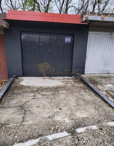 Garáž Púpavova, Karlova Ves + pivnica - Sivá garáž na ulici Púpavová, obklopená stromami, príjazdová cesta pred garážou.