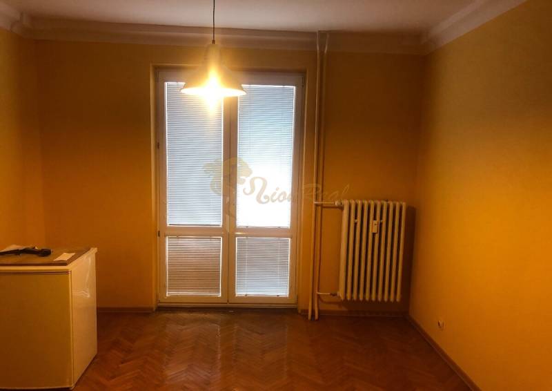 1-izb. byt na ul. Račianska, Nové Mesto s lodžiou - Žlté steny, podlaha s dreveným dekorom, radiátor a svetlo v 1-izbovom byte.