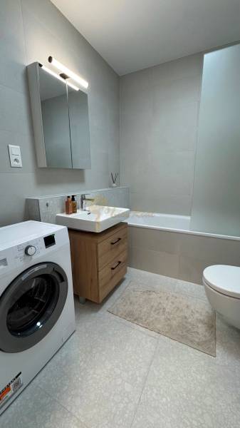 Novostavba 2,5-izb. bytu v NUPPU, garážové státie + vonkajšie státie - Kúpeľňa v 2-izbovom byte s vaňou, umývadlom, práčkou a skrinkou s dreveným dekorom.