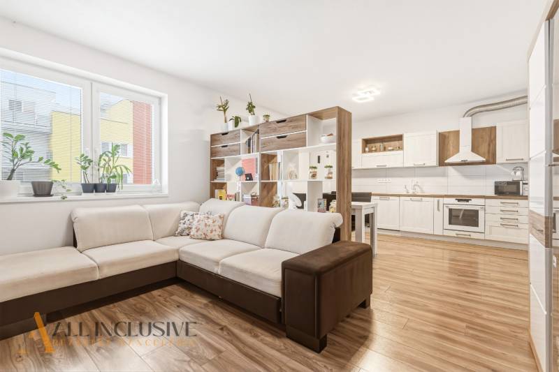 Na predaj moderný 2-izb. byt s loggiou vo Vrábľoch - Obývacia izba v 2-izbovom byte s veľkou sedačkou a kuchyňou, podlaha s dreveným dekorom.