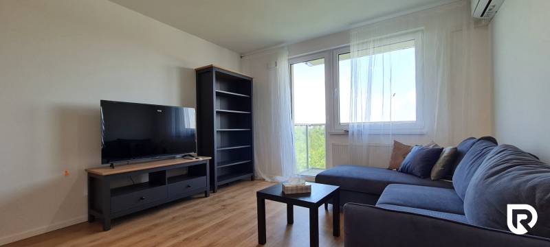 Zariadený 2-izb. byt v novostavbe v Ružinove - Ovocné sady - Obývacia izba v 2-izbovom byte s pohovkou, televízorom a podlahou s dreveným dekorom.