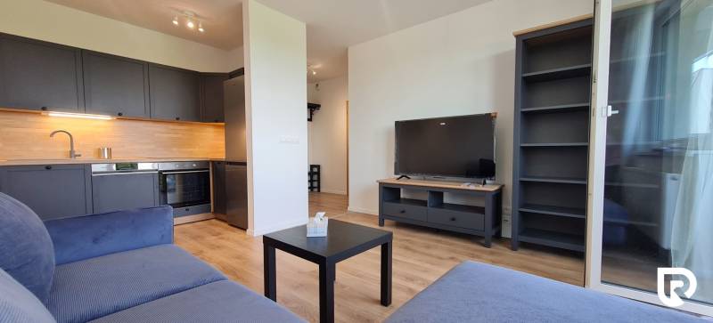 Zariadený 2-izb. byt v novostavbe v Ružinove - Ovocné sady - 2-izbový byt s kuchynskou linkou, modrým gaučom, televízorom a podlahou s dreveným dekorom.