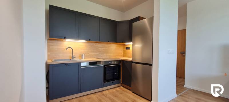 Zariadený 2-izb. byt v novostavbe v Ružinove - Ovocné sady - Kuchyňa v 2-izbovom byte s tmavosivými skrinkami, dreveným dekorom a nerezovými spotrebičmi.