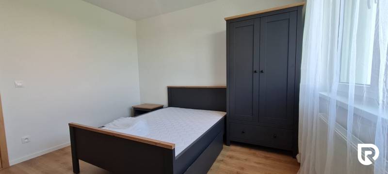 Zariadený 2-izb. byt v novostavbe v Ružinove - Ovocné sady - Spálňa v 2-izbovom byte obsahuje posteľ, nočný stolík, šatník a podlahu s dreveným dekorom.