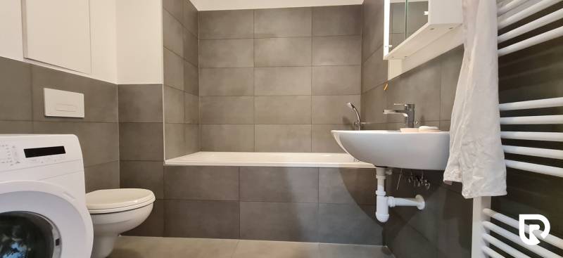 Zariadený 2-izb. byt v novostavbe v Ružinove - Ovocné sady - Kúpeľňa s vaňou, umývadlom a práčkou v 2-izbovom byte. Šedé obkladačky dominujú priestoru.