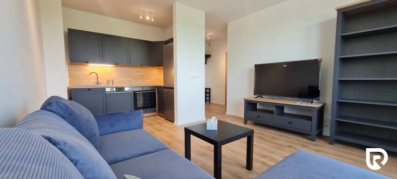 Zariadený 2-izb. byt v novostavbe v Ružinove - Ovocné sady - Obývacia izba s kuchynským kútom, šedou pohovkou a podlahou s dreveným dekorom v 2-izbovom byte.