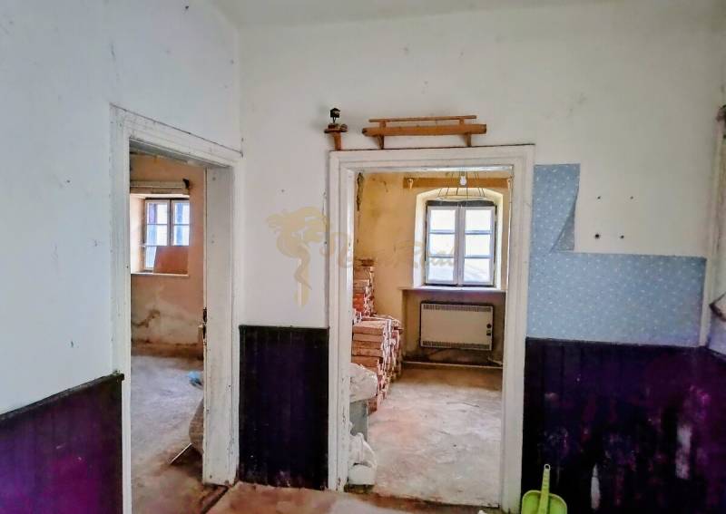 Rodinný dom Svätý Jur, centrum, pôvodný stav - Interiér rodinného domu s dreveným dekorom a starším zariadením, biele steny, okná.