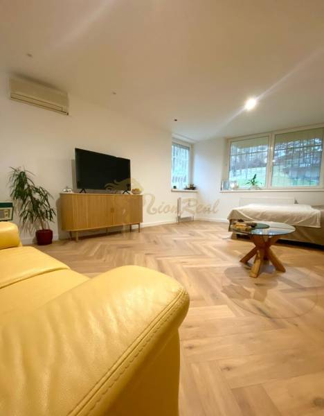 4-izb. byt, Cabanova ul., Dúbravka so samostatným vstupom - Obývacia izba so žltou sedačkou, TV a dreveným stolom v 4-izbovom byte na ulici Cabanova.