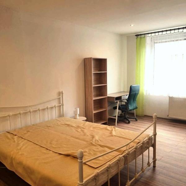 Pekný 2 izbový byt na prenájom - Malacky - Spálňa s posteľou, stolom, policou a podlahou s dreveným dekorom v 2-izbovom byte.