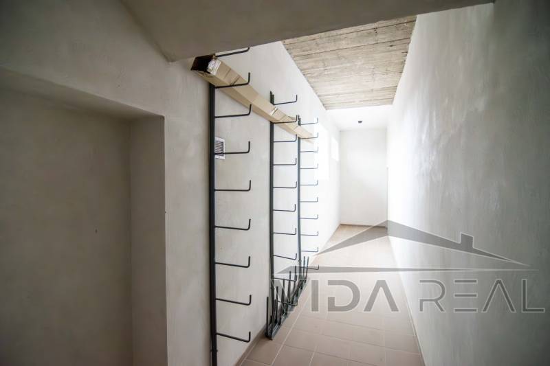 Prenájom haly / obchodno-skladových priestorov – Šenkvice, Nádražná ul - Úzky interiérový priestor v sklade s kovovými vešiakmi na stene.