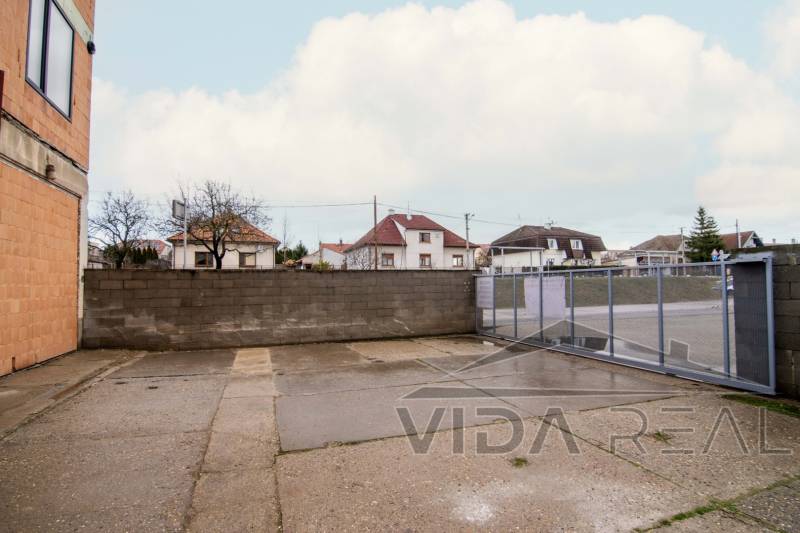 Prenájom haly / obchodno-skladových priestorov – Šenkvice, Nádražná ul - Exteriér na Nádražnej ulici v Šenkviciach, vedľa skladov a hál s oceľovou bránou.